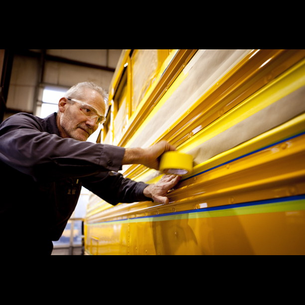 Tech applying tape before painting bus