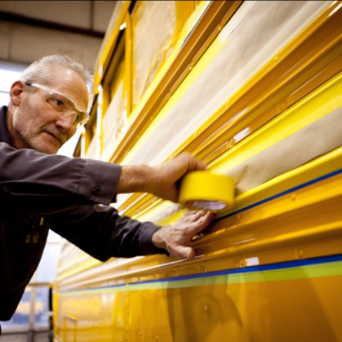 Tech applying tape before painting bus